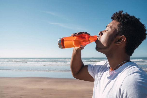 Portrait of an athletic man drinking something after training at the beach. Sport and health lifestyle. - Foto, Imagen