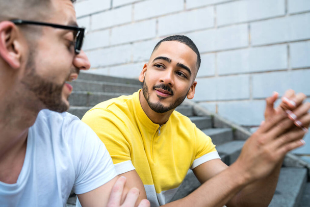 Portrait of happy gay couple spending time together while sitting on stairs outdoors. Lgbt and love concept. - Foto, Bild