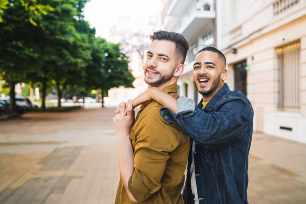 Portrait of happy gay couple spending time together and hugging in the street. Lgbt and love concept. - 写真・画像