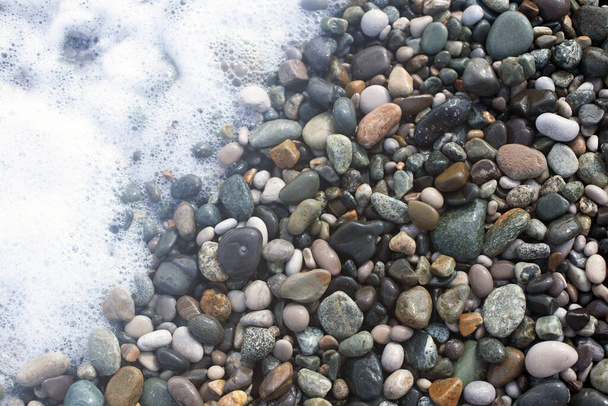 Υγρό λείο γυαλιστερό θαλασσινό βότσαλο και λευκό θαλασσινό αφρό close up φόντο σε φυσικά χρώματα - Φωτογραφία, εικόνα