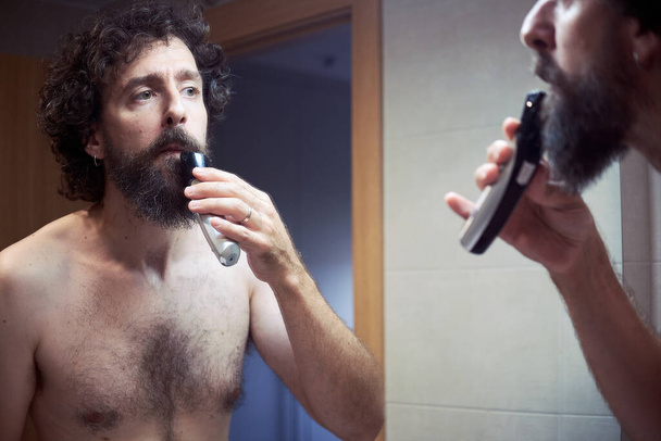 Homem hispânico de meia-idade cortando sua barba - Foto, Imagem