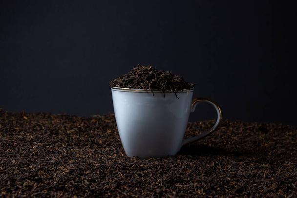 Loose tea on a black background. White cup on a heap of loose tea. - Photo, Image