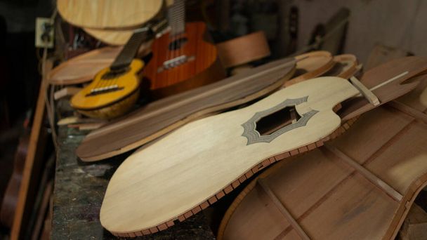 Чаранго и гитара из красного дерева на стопке несмонтированных гитарных деталей на столярном столе в мастерской - Фото, изображение