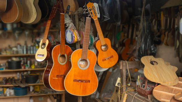 Загальний вигляд гітарної майстерні з підвішеними дерев'яними гітарами і безліччю незбираних деталей на столярному столі з задніми стінами, наповненими інструментами
 - Фото, зображення