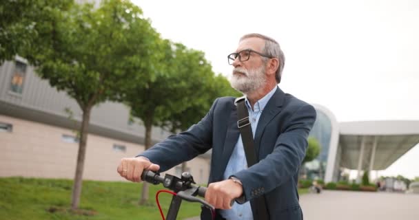 Muotokuva valkoihoinen vanha mies harmaat hiukset ja lasit istuu pyörä ja katselee kameraa. Vanhempi harmaa-tukkainen isoisä sähköskootterilla ulkona. Miespuolinen eläkeläinen pyörällä kaupungissa. - Materiaali, video
