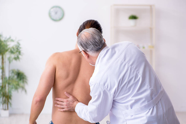 Joven hombre lesionado de espalda visitando experimentado médico masculino
 - Foto, Imagen
