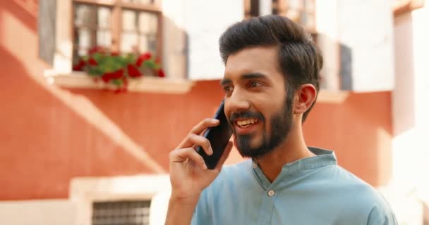 Hindoe jonge knappe glimlachte man buiten staan op straat op zonnige dag en praten op mobiele telefoon. Een man uit India die op een mobieltje spreekt en buiten lacht. Telefoon bellen. - Video