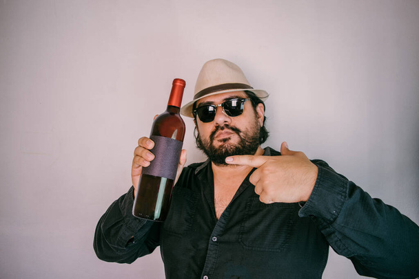 Латиноамериканець з панамським капелюхом, що показує пляшку вина з порожньою етикеткою. Виноградна пляшка. - Фото, зображення