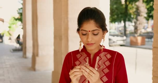 Hindoe jonge mooie vrouw met rode stip op het voorhoofd en in traditionele outfit ruiken parfum buiten. Stijlvolle charmante vrouwelijke snuiven geur en aroma op straat. Schoonheidsconcept. Parfum. - Video