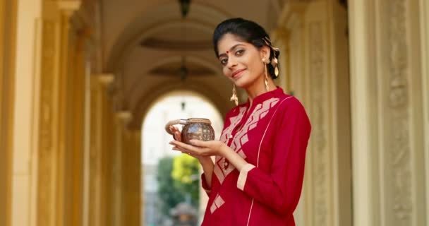 Alnında nokta olan, geleneksel kırmızı elbiseli, binadaki kameraya gülümseyen ve içinde mum olan lambayı tutan Hindu genç ve güzel bir kadının portresi. Kültür ve gümrük kavramı. - Video, Çekim