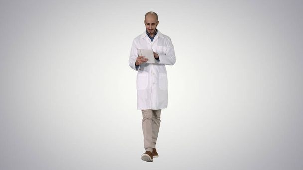 Mature male doctor holding digital tablet using it and walking o - Фото, изображение