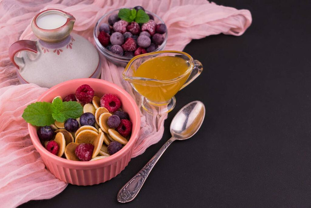 Frühstück aus kleinen Pfannkuchen mit Beeren und Honig auf schwarzem Hintergrund.. - Foto, Bild