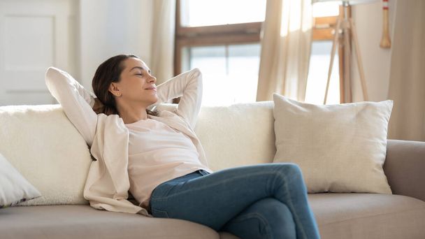 Confident millennial female enjoying tranquility relaxing on sofa indoors - Фото, изображение