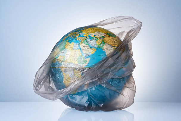 The concept of protecting the world from plastic waste, fighting environmental pollution, fighting for the environment, a globe in a black garbage bag on a light background. No plastic bags. - Фото, зображення