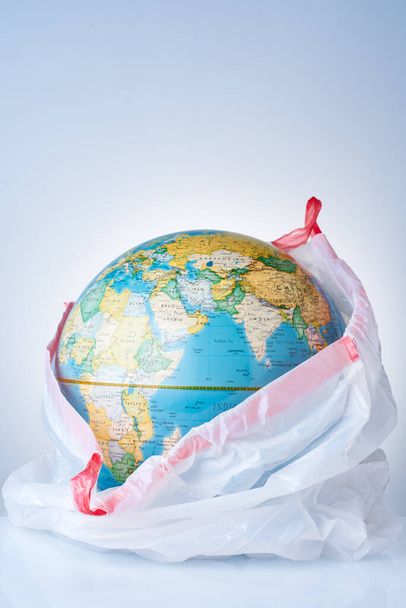 The concept of protecting the world from plastic waste, fighting environmental pollution, fighting for the environment, a globe in a white garbage bag on a light background. No plastic bags - Photo, Image