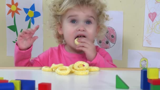 Tyttö syö maissia pöydällä. Sympaattinen kihara tyttö, jolla on siniset silmät. 4K - Materiaali, video