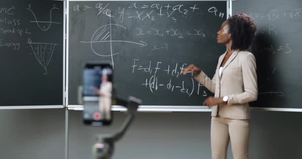 学校でのスマートフォン録画ビデオレッスン。オンライン学習。アフリカ系アメリカ人の若い女性教師が授業で数学や物理式を説明する。隔離の概念。インターネットによる研究。隔離. - 映像、動画