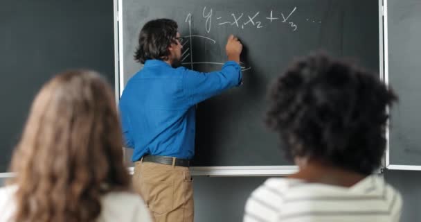 Caucasian man leraar op school schrijven formules en wiskunde wetten op schoolbord. Schoolconcept. Man docent in bril die wiskunde wetten uitlegt aan leerlingen. Onderwijsconcept. - Video