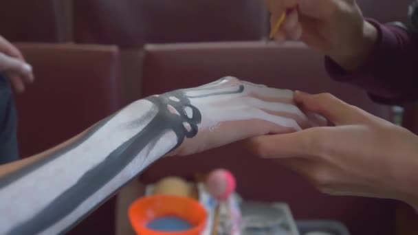 Mom paints the girl's hands with white and black paint. The skeleton print on the body.  preparing for Halloween. - Footage, Video