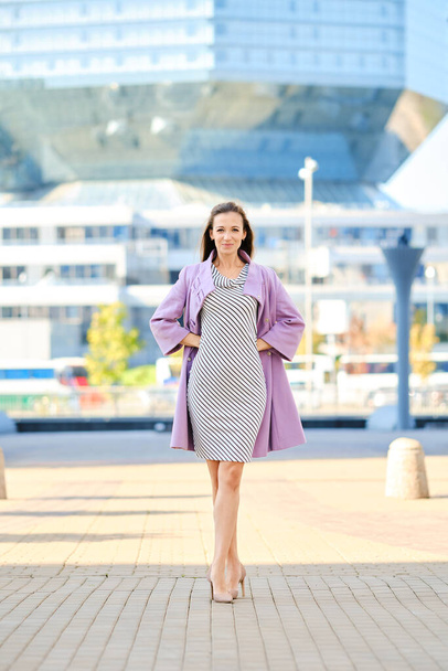Trendy woman in lilac coat and striped dress posing outdoor - Φωτογραφία, εικόνα