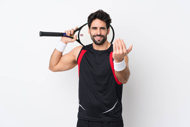 Młody przystojny mężczyzna z brodą na białym tle gra w tenisa i robi nadchodzący gest - Zdjęcie, obraz