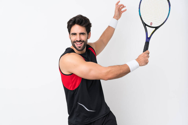 Junger gutaussehender Mann mit Bart über isoliertem weißem Hintergrund spielt Tennis - Foto, Bild