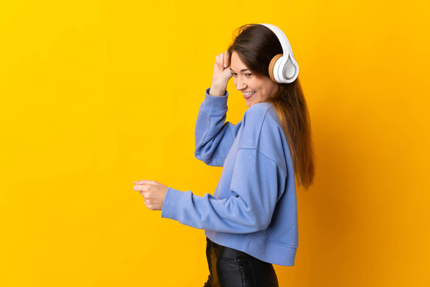Junge Irin isoliert auf gelbem Hintergrund Musik hören und tanzen - Foto, Bild