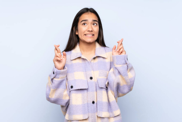 Young Indian woman isolated on blue background with fingers crossing and wishing the best - Photo, Image