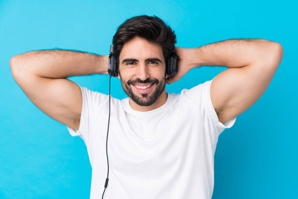 Jovem homem bonito com barba sobre fundo azul isolado ouvindo música - Foto, Imagem