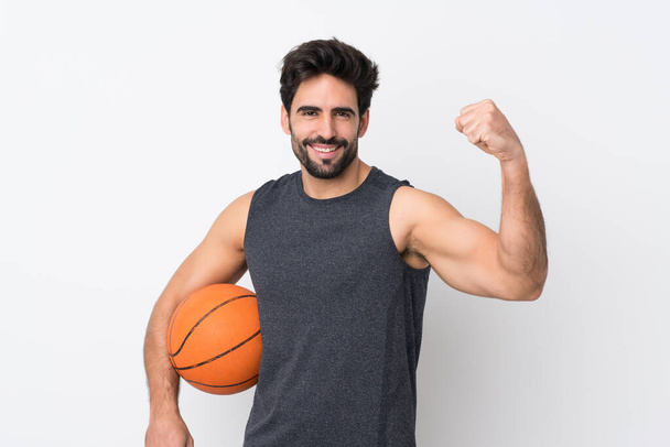 Молодой красивый мужчина с бородой на изолированном белом фоне играет в баскетбол и гордится собой - Фото, изображение
