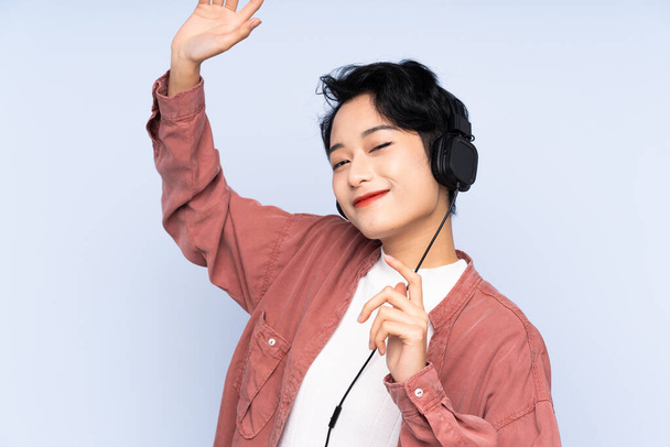 Młoda Azjatka nad odizolowanym niebieskim tle słuchanie muzyki i tańca - Zdjęcie, obraz