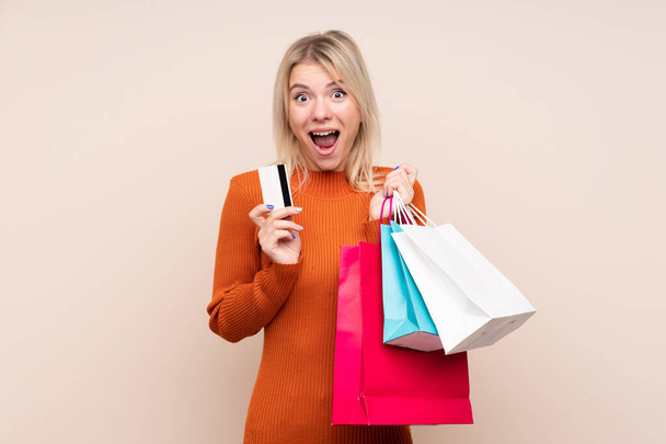 Jonge blonde vrouw over geïsoleerde achtergrond holding shopping tassen en verrast - Foto, afbeelding
