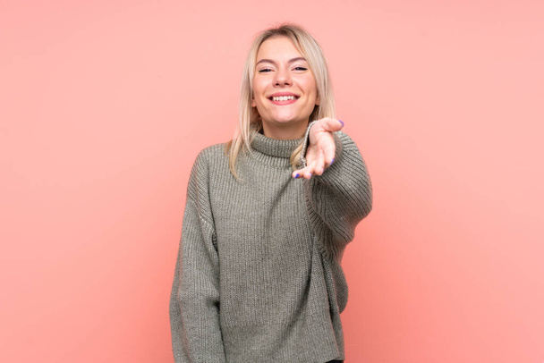 Young blonde Russian woman over isolated pink background shaking hands for closing a good deal - Photo, Image