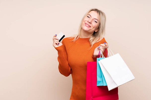 Young blonde woman over isolated background holding shopping bags and a credit card - Foto, Imagem