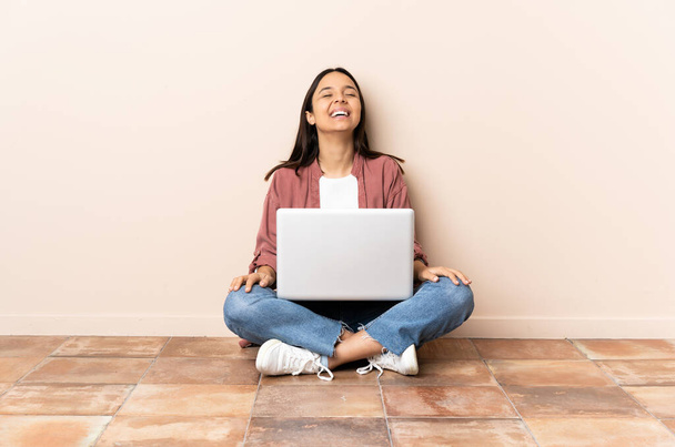 jong gemengd ras vrouw met een laptop zitten op de vloer lachen - Foto, afbeelding