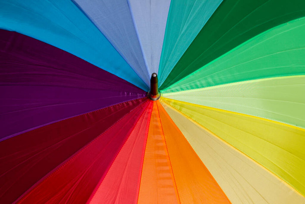 Un paraguas multicolor con rayas en colores arco iris, un símbolo de la bandera LGBT. - Foto, Imagen