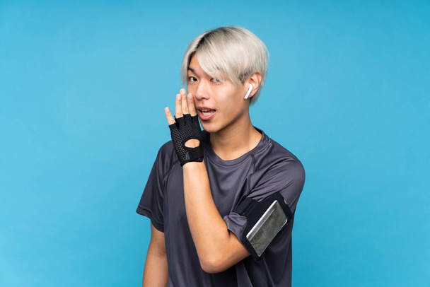 Young asian sport man over isolated blue background whispering something - Фото, зображення