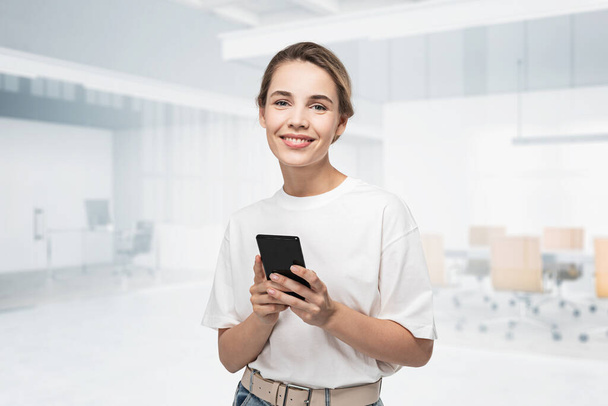 Portrait of smiling young woman in casual clothes using smartphone in blurry office. Concept of communication. toned image double exposure - Фото, изображение