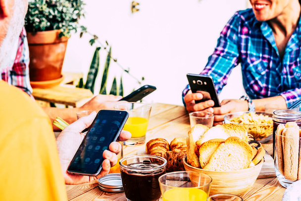 Close up de grupo de pessoas usam telefone na mesa enquanto tomam café da manhã juntos  - Foto, Imagem