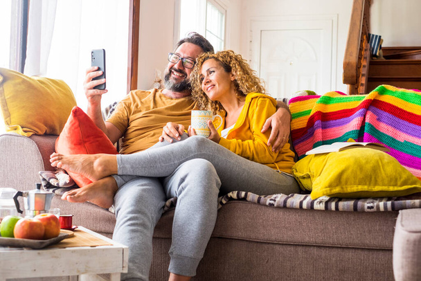 Joyeux et joyeux beau couple adulte faire une vidéoconférence en utilisant la connexion téléphonique en ligne à la maison pendant le petit déjeuner du matin ensemble - Photo, image