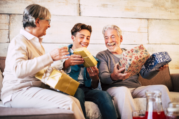 Ευτυχισμένη οικογένεια την παραμονή των Χριστουγέννων με παππούδες και εγγονό έφηβος διασκεδάζουν με ανταλλαγή δώρων δραστηριότητα στο σπίτι στον καναπέ  - Φωτογραφία, εικόνα