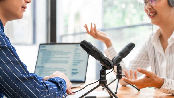 Asian woman radio hosts gesturing to microphone while interviewing a man guest in a studio while recording podcast for online show in studio together. - 写真・画像