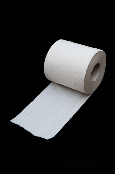 Eine Rolle entrolltes weißes Toilettenpapier. Vereinzelt auf schwarzem Hintergrund. Nahaufnahme. Kopierraum. Vertikaler Schuss. - Foto, Bild