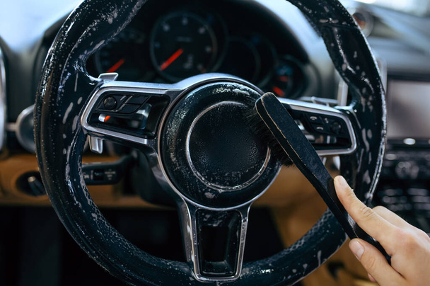 Trabalhador com escova limpa o volante do carro, limpeza a seco e detalhamento. Lavagem de veículos na garagem, cuidado completo do automóvel, produto químico e serviço limpo - Foto, Imagem