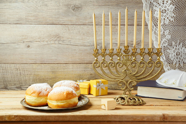 Jewish holiday Hanukkah concept with menorah, sufganiyah, gift box and spinning top on wooden table - Fotó, kép
