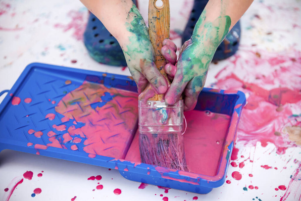 children hands hold a brush in pink paint on a background of paper stained with paint - 写真・画像