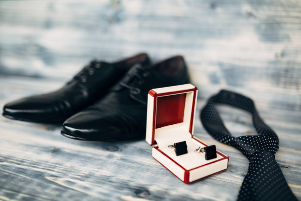 Chaussures homme en cuir noir avec boutons de manchette et cravate à pois sur la texture du bois avec une faible profondeur de champ. - Photo, image