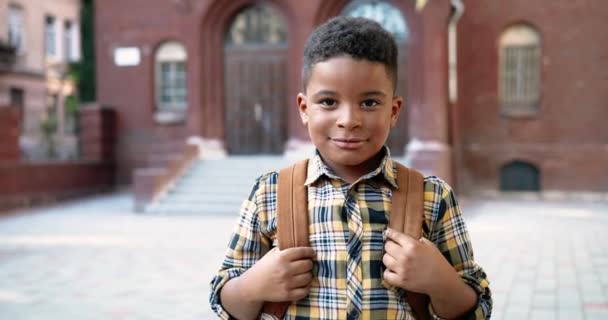 Okul bahçesinde kameraya gülümseyen Afro-Amerikan erkek öğrenci portresini yakından çek. Okulun yanındaki neşeli çocuk sırt çantasıyla keyfi yerinde. Konsept çalış - Video, Çekim