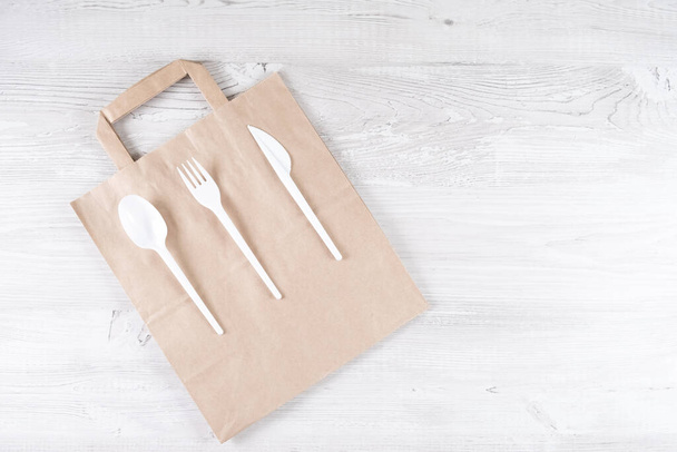 plastic fork, spoon, knife on paper bag. Eco-friendly food packaging and cotton eco bags on gray background with copy space. Carering of nature and recycling concept. containers for catering and - Foto, imagen