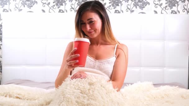funny female sitting in bed with takeaway coffee, enjoying the morning and drinking coffee. The concept of starting a new day, relaxing on the weekend, no need to rush anywhere, good morning - Footage, Video